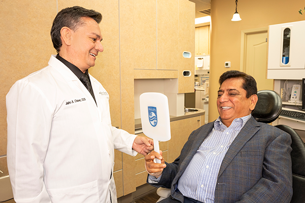 A patient looks at his smile on a small mirror while Dr. Chavez looks on